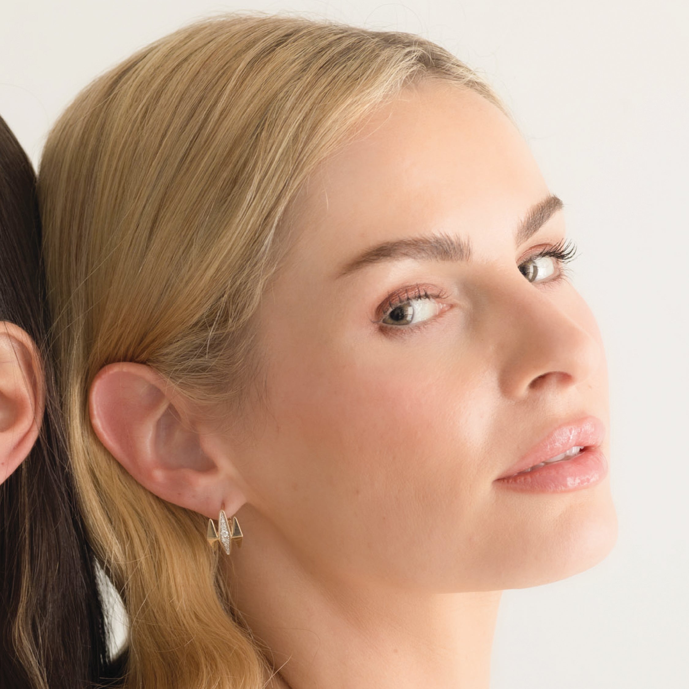 Woman wearing 14K solid gold diamond earrings with a geometric design.
