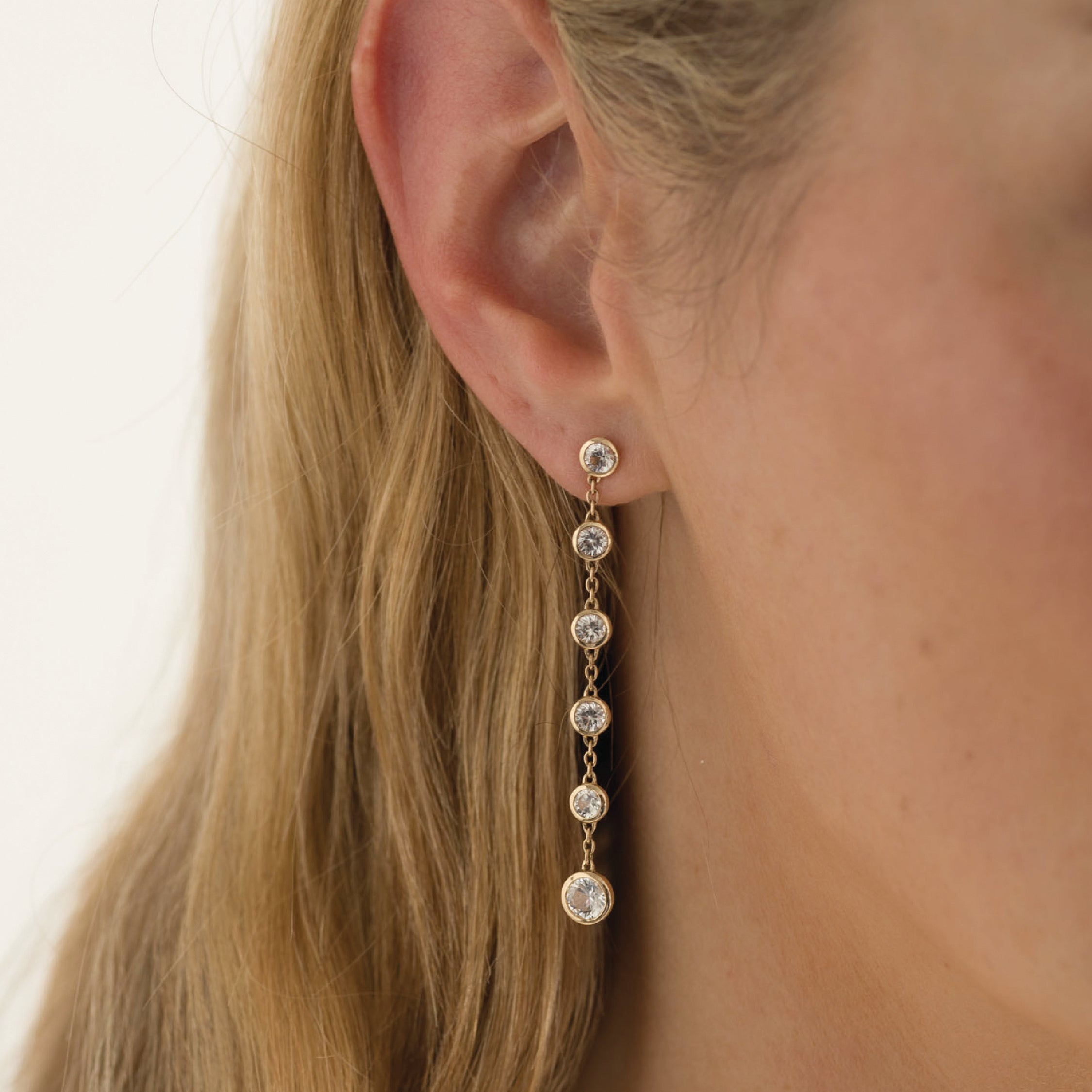 14K gold earrings with white sapphire gemstones in a long drop style.