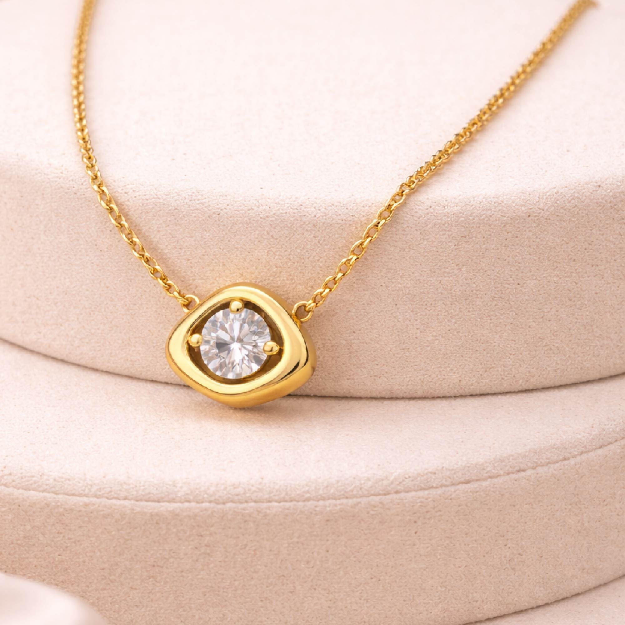 Gold necklace with a diamond pendant on a beige cushion