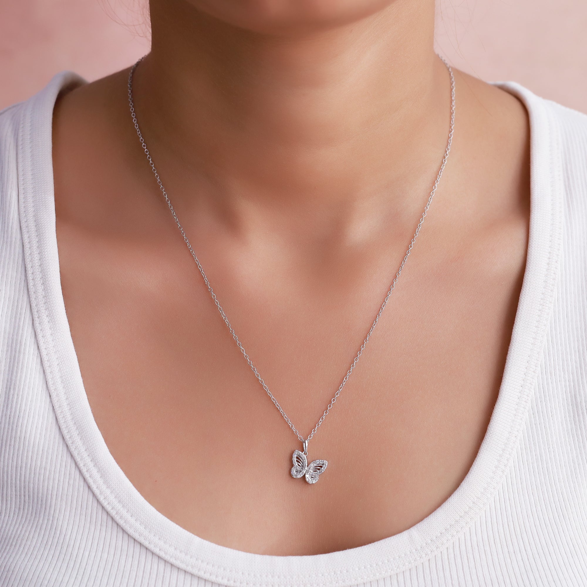 Silver butterfly necklace on a model wearing a white top against a pink background