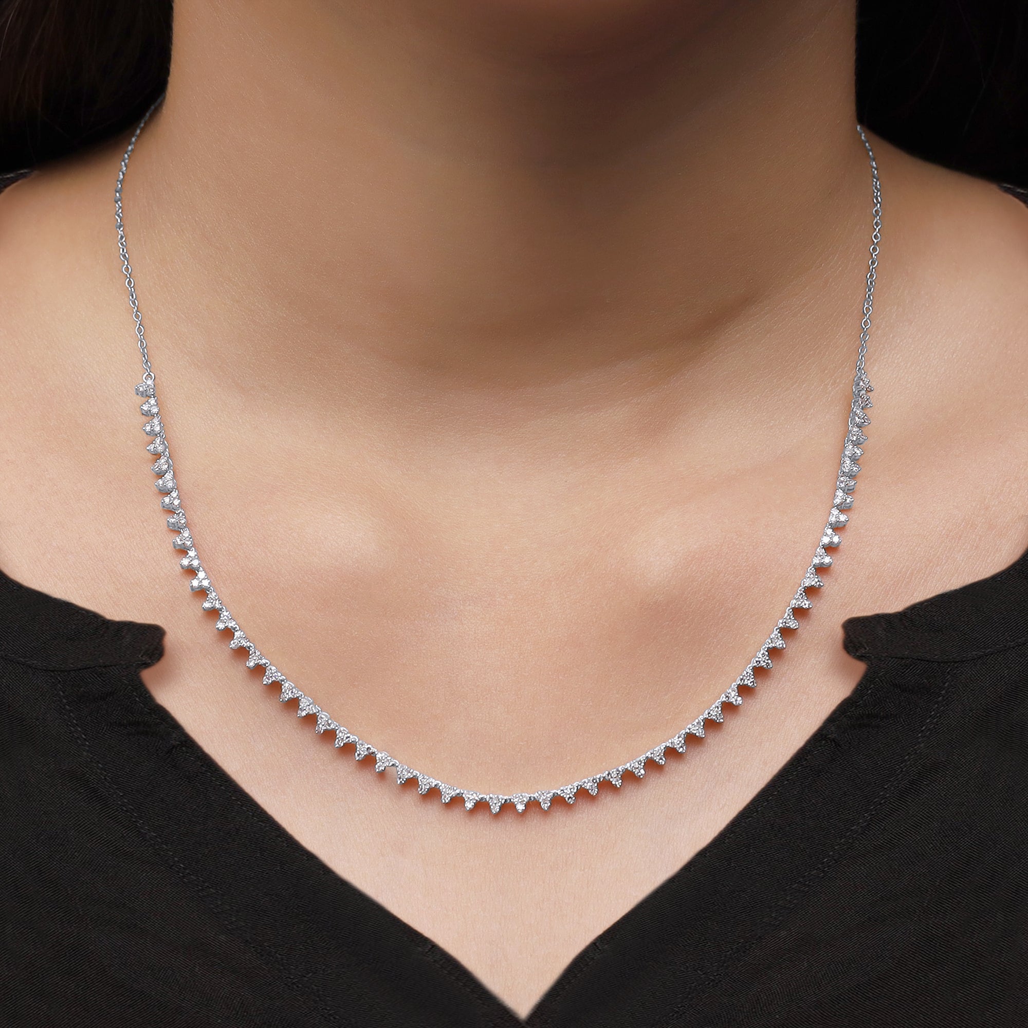 Silver necklace on a person wearing a black top against a black background