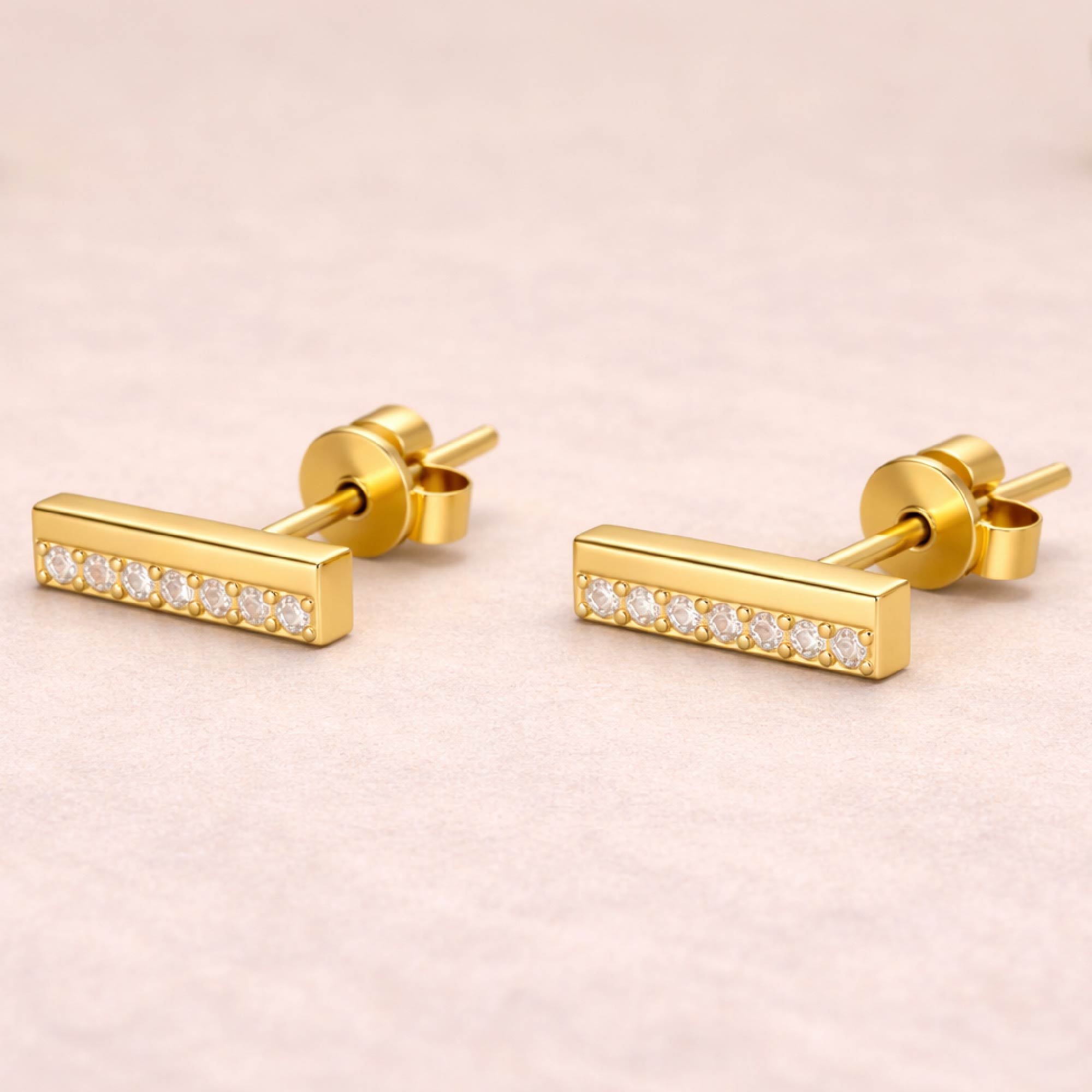 Gold bar earrings with embedded diamonds on a light pink background