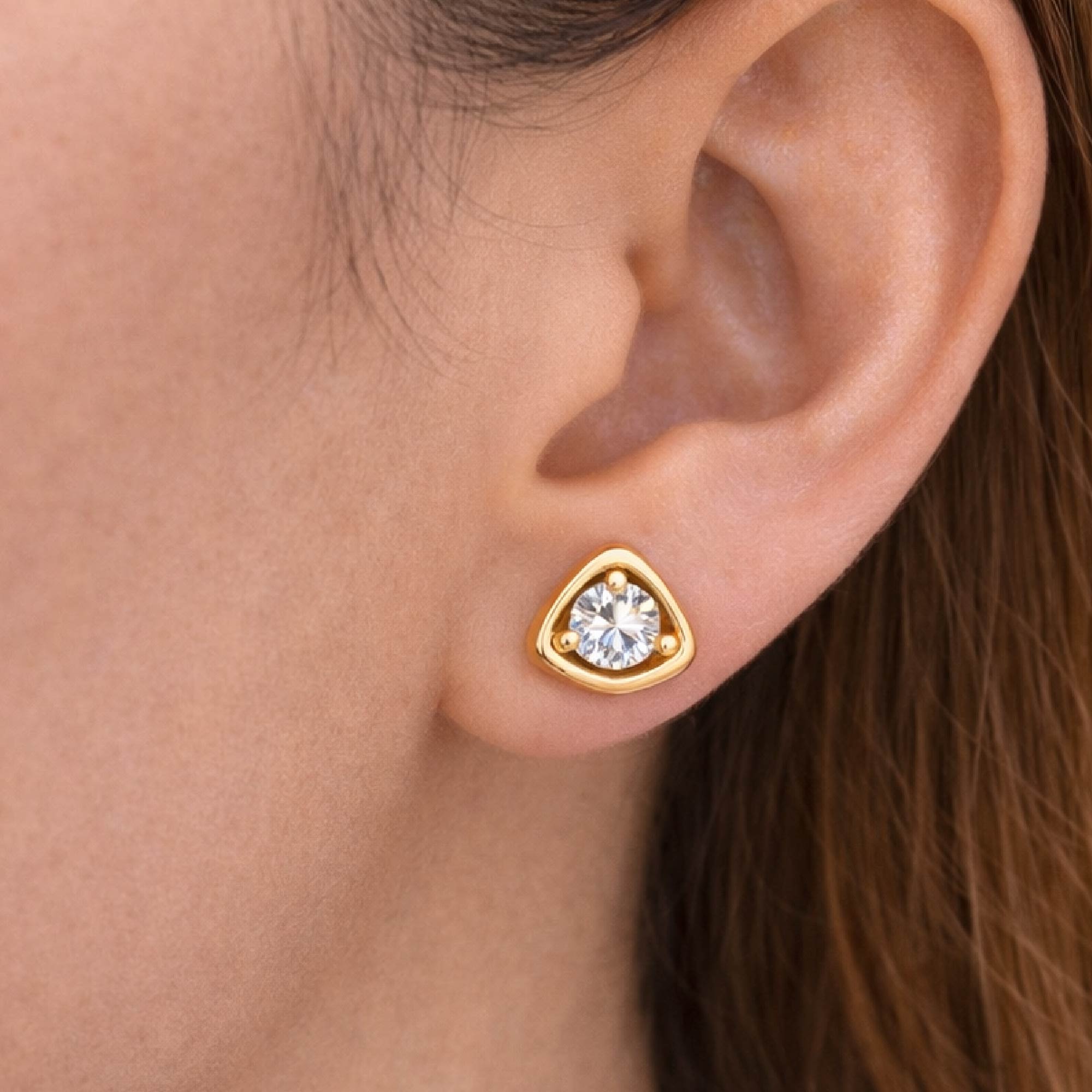 Gold earring with a clear gemstone worn by a person