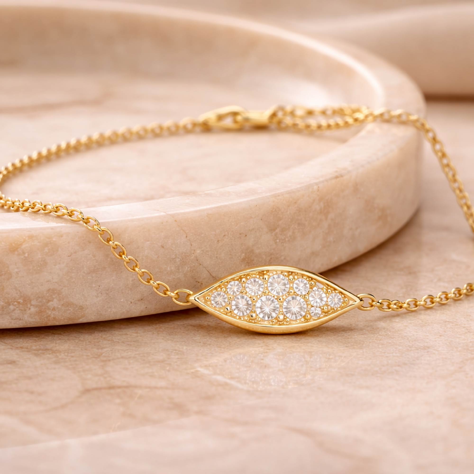 Gold bracelet with diamond-studded evil eye design on a beige marble surface