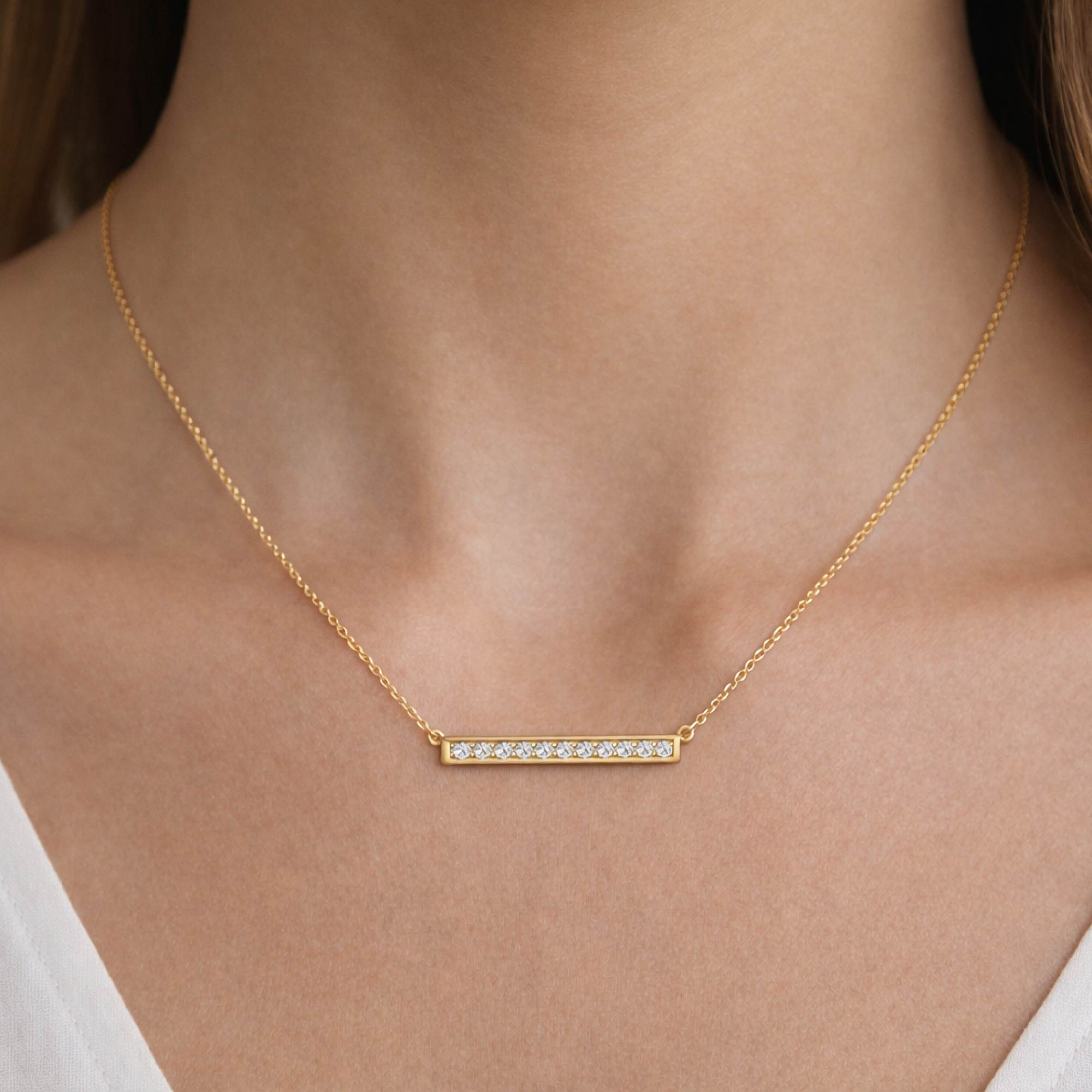 Gold necklace with a bar pendant on a person wearing a white top.