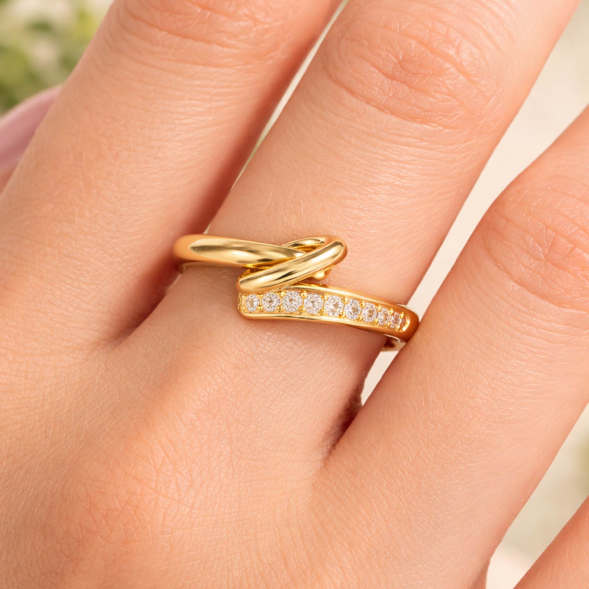Gold ring with diamonds on a finger against a neutral background