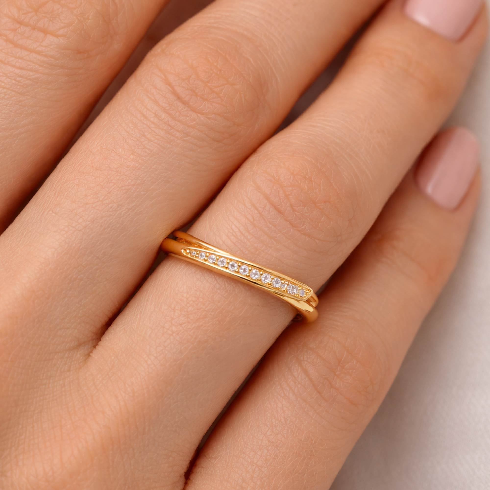 Gold ring with small diamonds on a person's finger against a neutral background