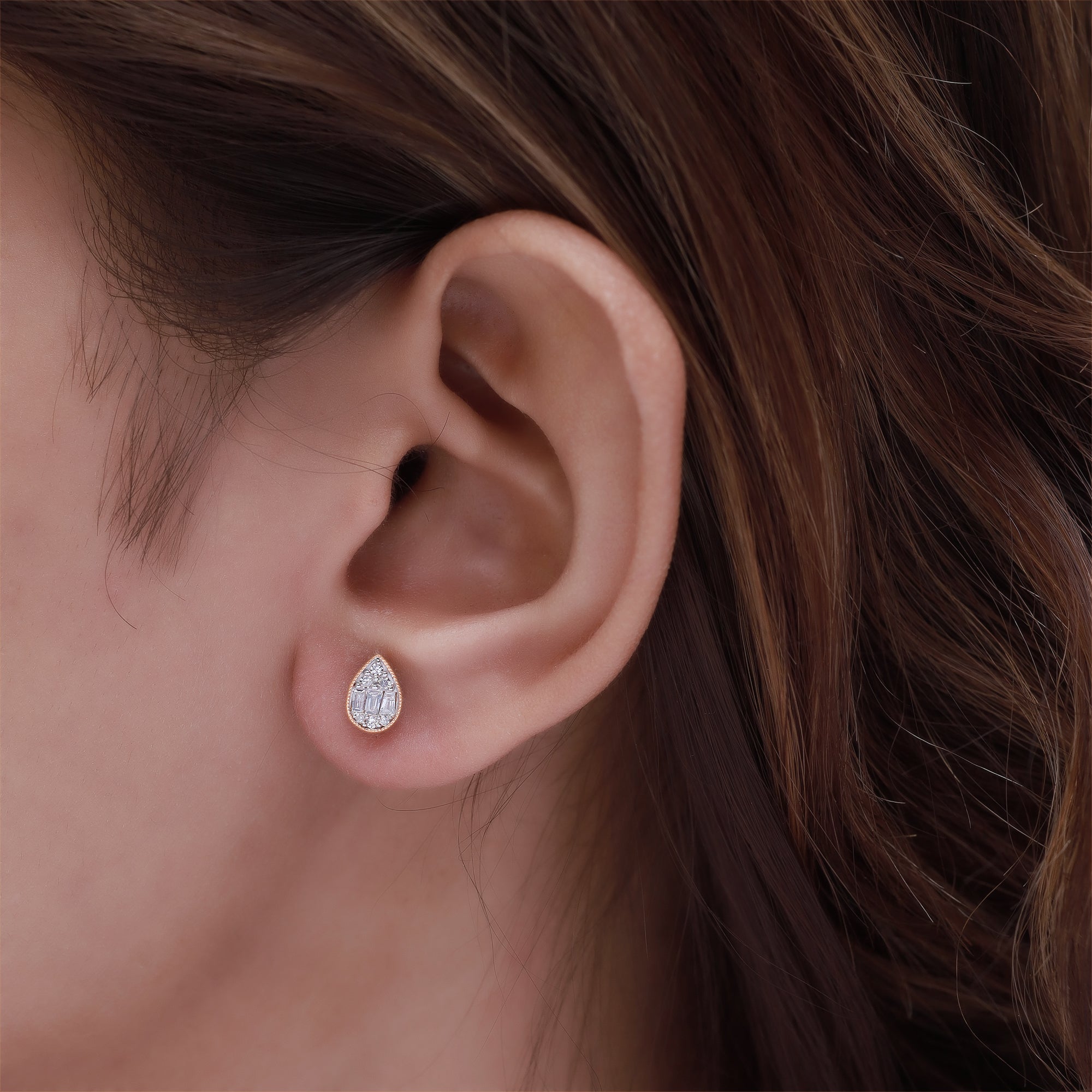 Close-up of an ear wearing a diamond earring with brown hair.