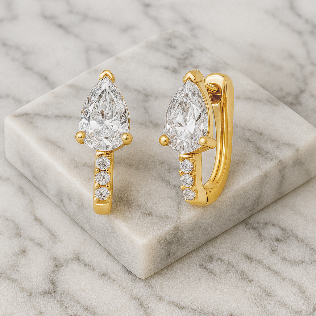 Gold earrings with pear-shaped diamonds on a marble surface
