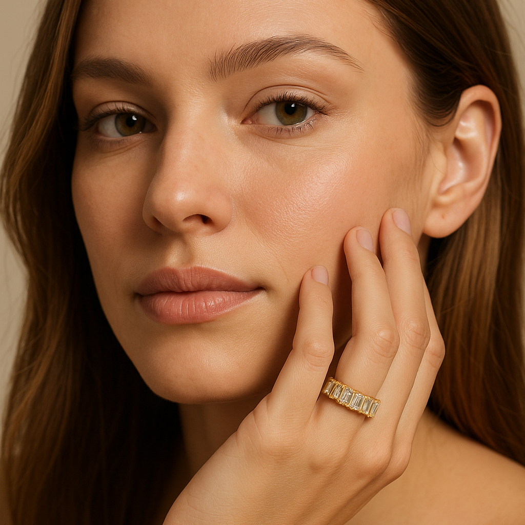 Woman with a gold ring on her finger touching her face against a neutral background