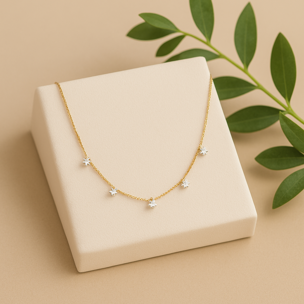 Gold necklace with star-shaped pendants on a beige box with green leaves in the background