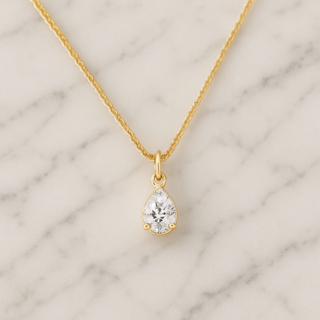 Gold necklace with a teardrop-shaped diamond pendant on a marble background