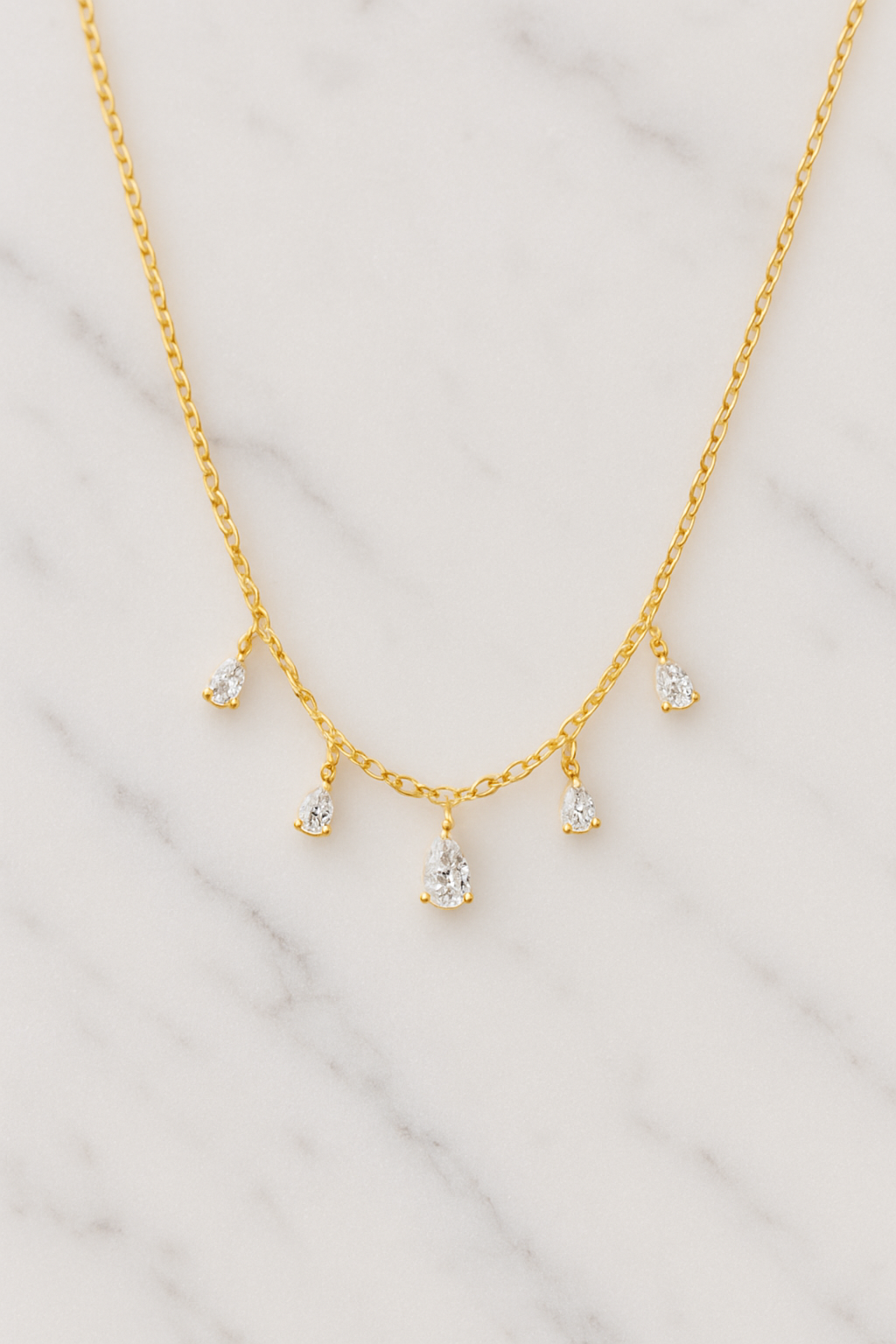 Gold necklace with small diamond-like pendants on a marble surface