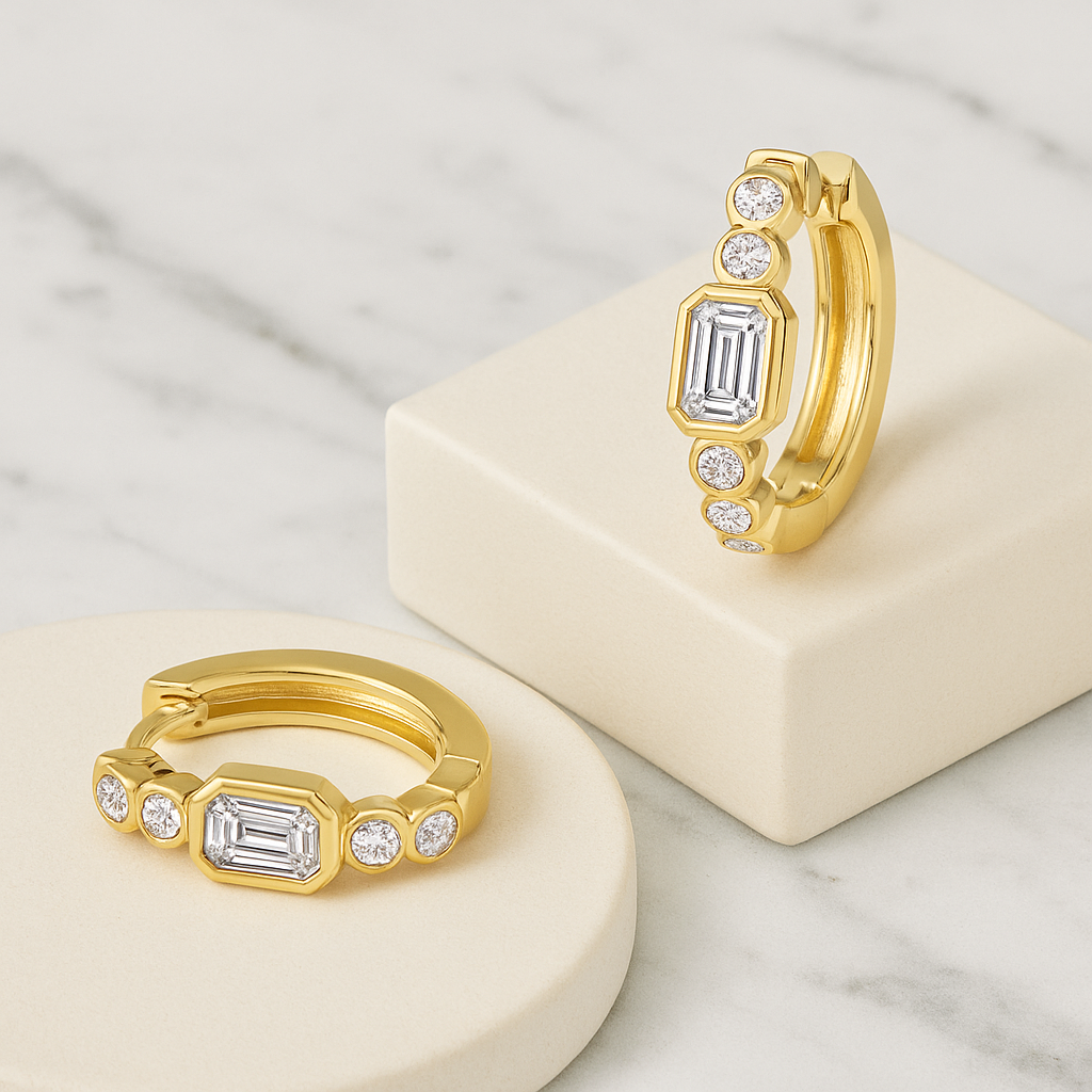 Two gold earrings with emerald-cut gemstones on a marble surface