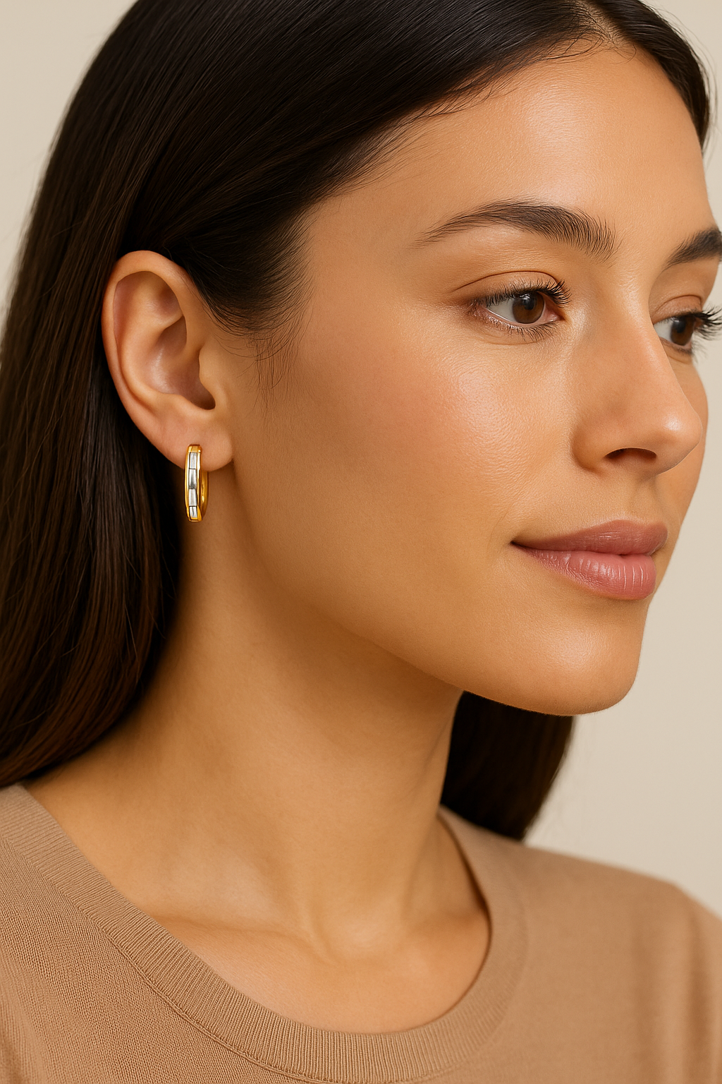 Close-up of a woman wearing gold hoop earrings against a neutral background
