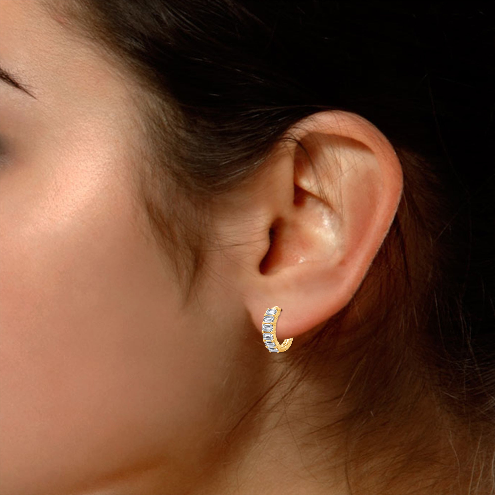 Gold hoop earrings with small diamonds worn by a person.
