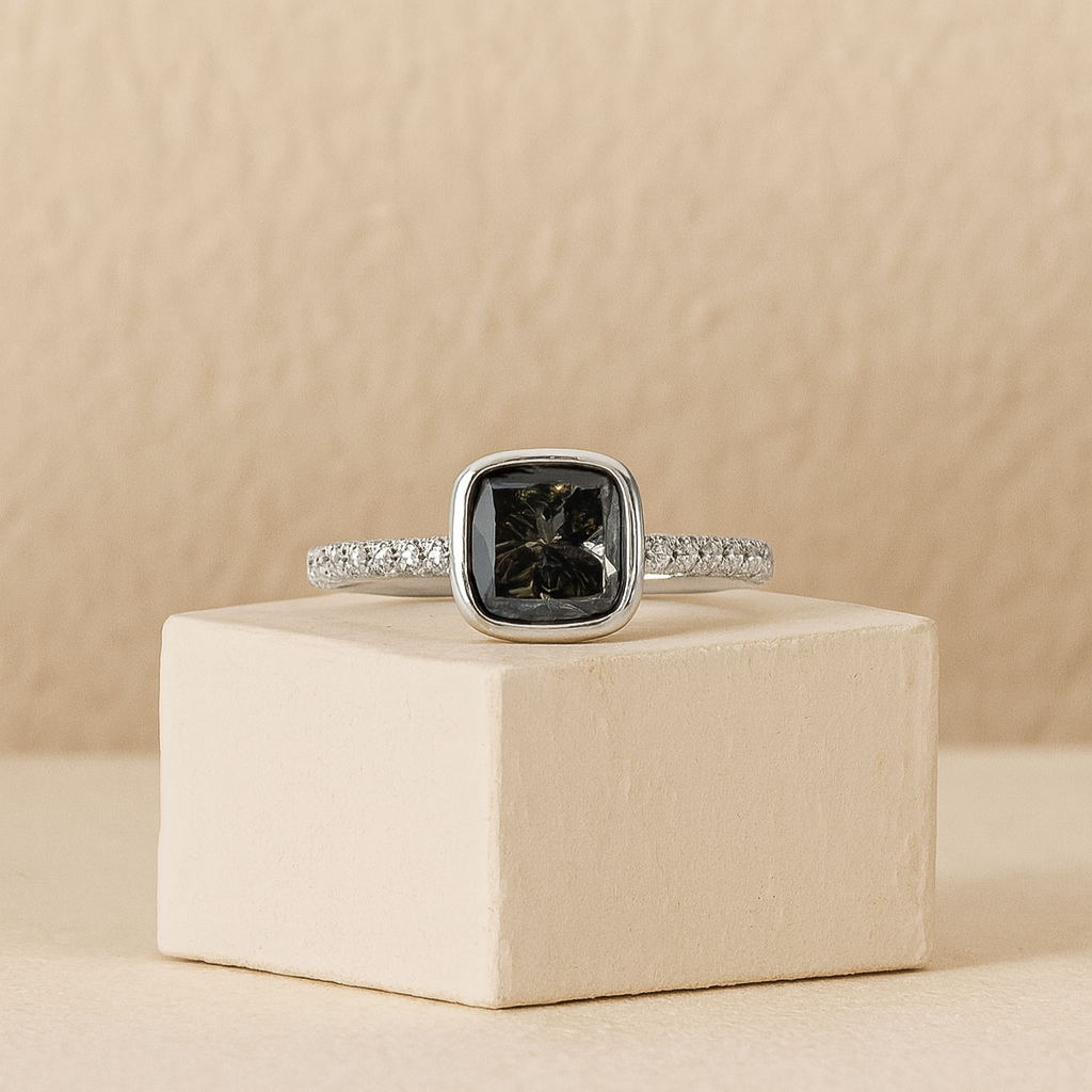 Silver ring with a dark gemstone on a beige cube against a beige background