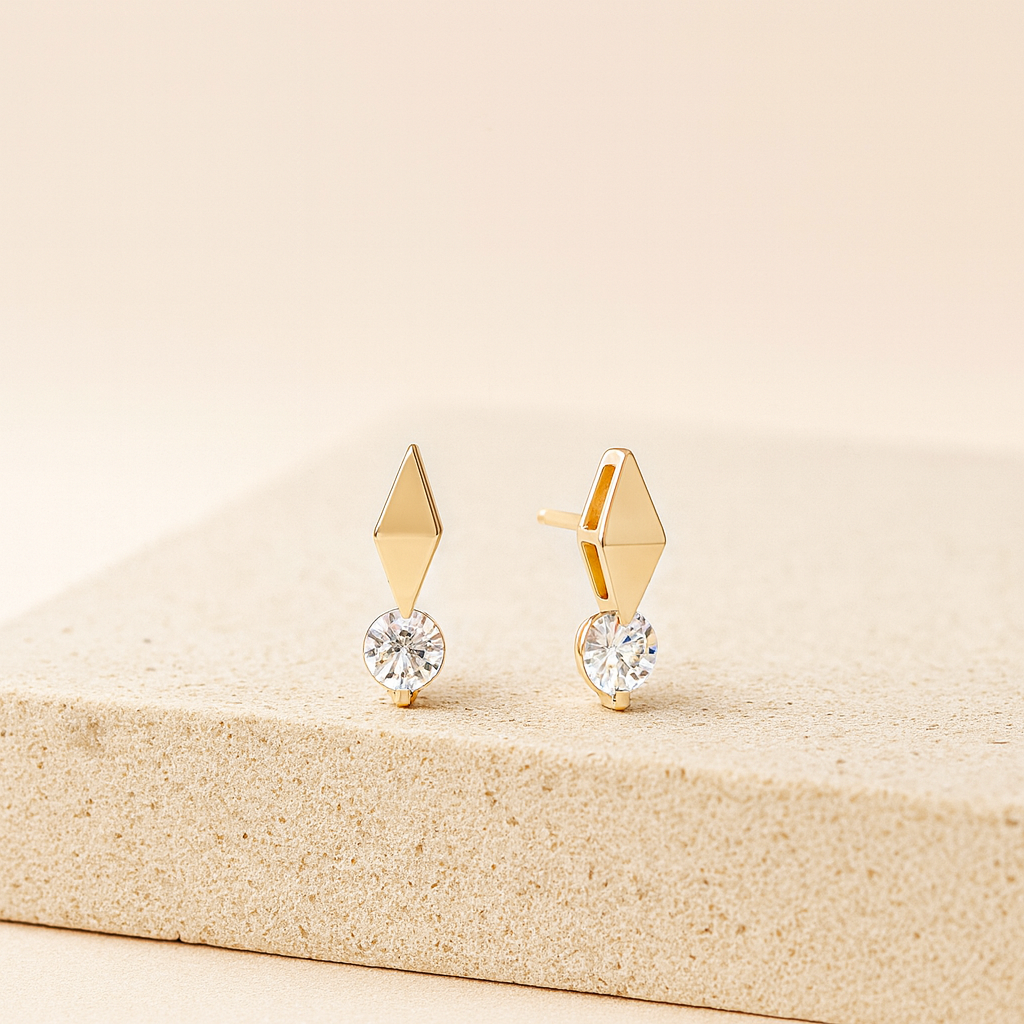 Gold earrings with diamond-like stones on a beige surface