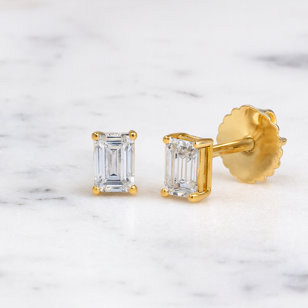 Gold earrings with emerald-cut gemstones on a marble background