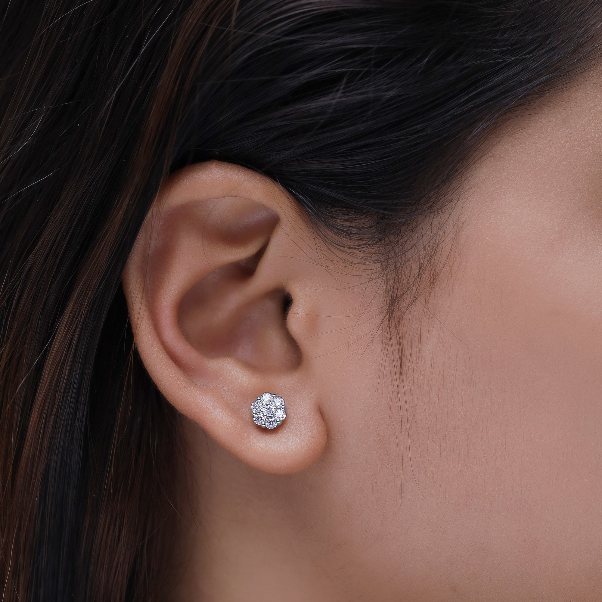Close-up of an ear wearing a diamond stud earring with dark hair.