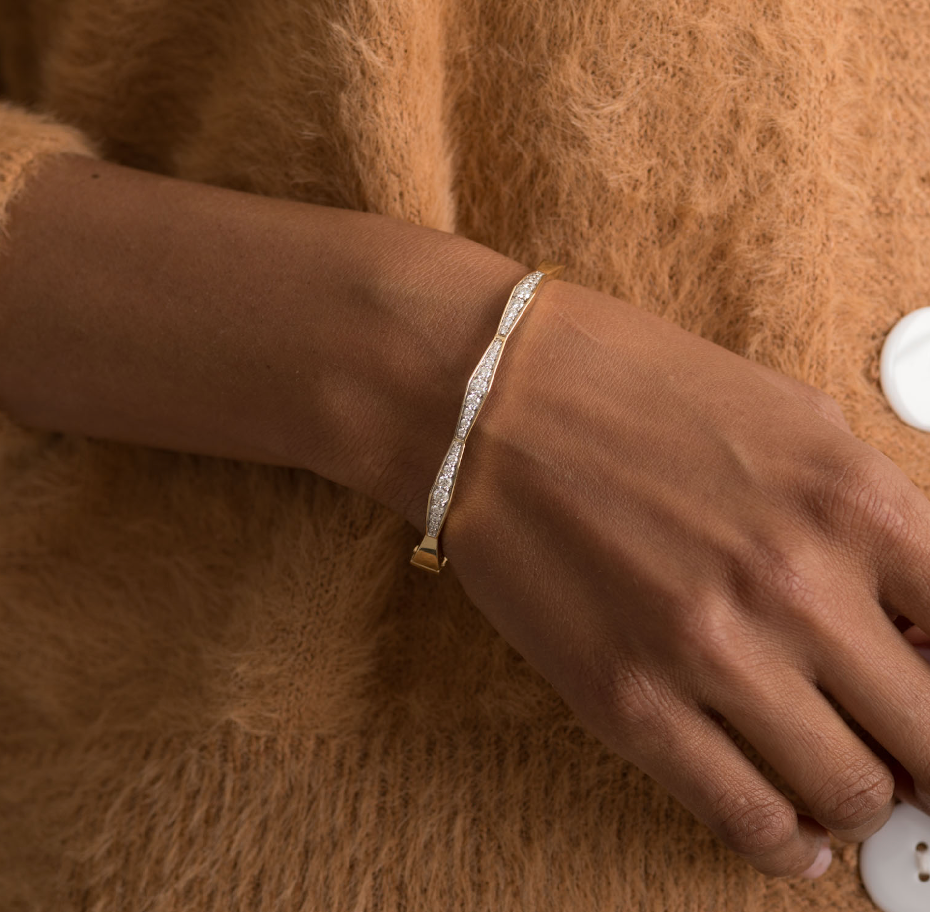 14K solid gold diamond bangle bracelet on wrist, featuring a twisted design with sparkling diamonds.