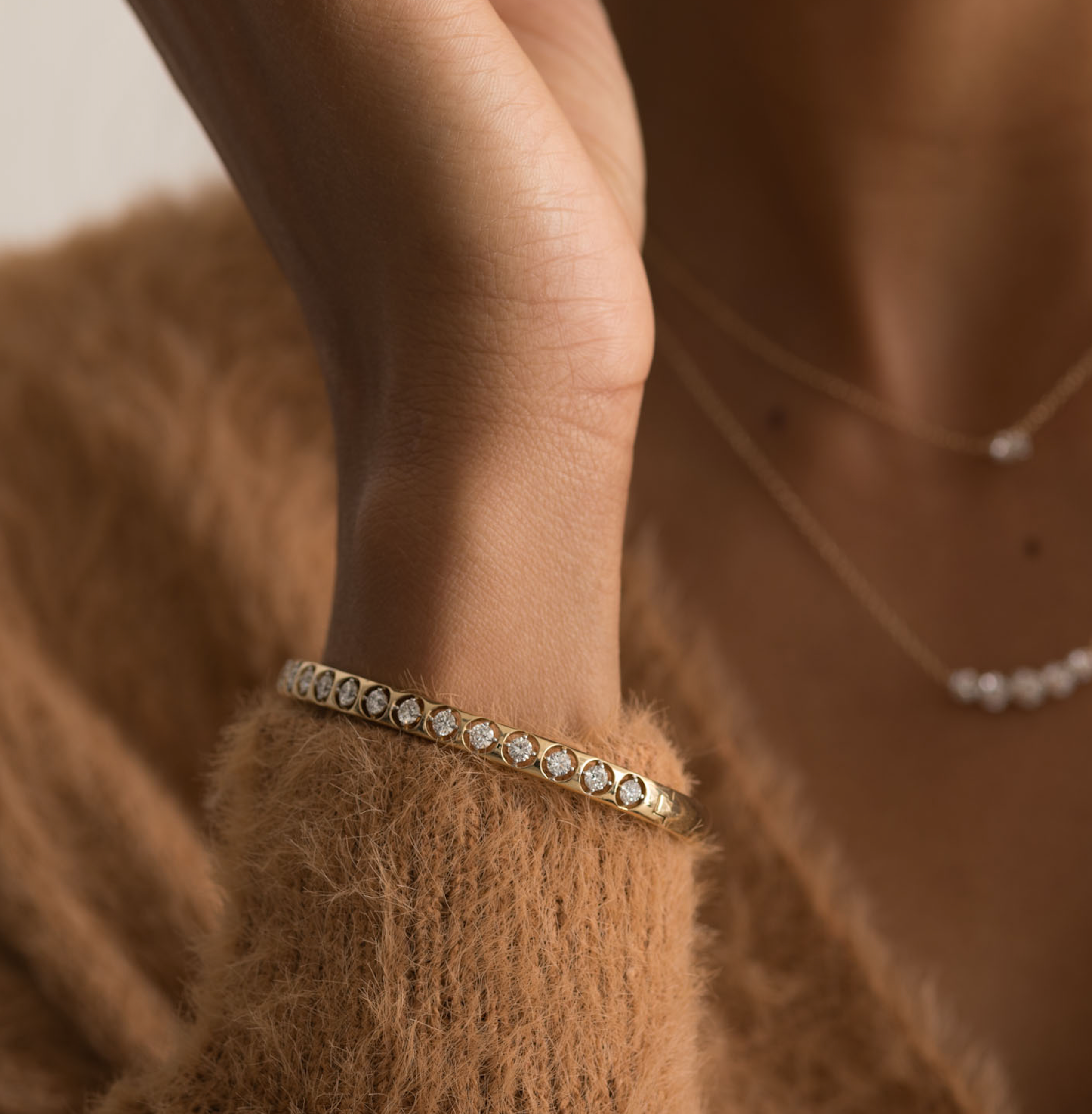 14K gold bangle bracelet with diamonds on wrist, worn with brown sweater.