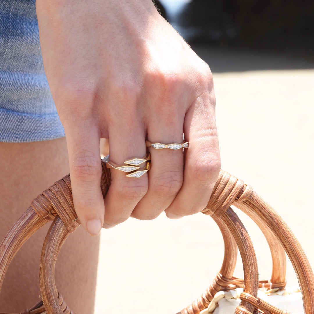 Hand wearing 14K gold diamond ring with triple bypass design, holding wicker bag.