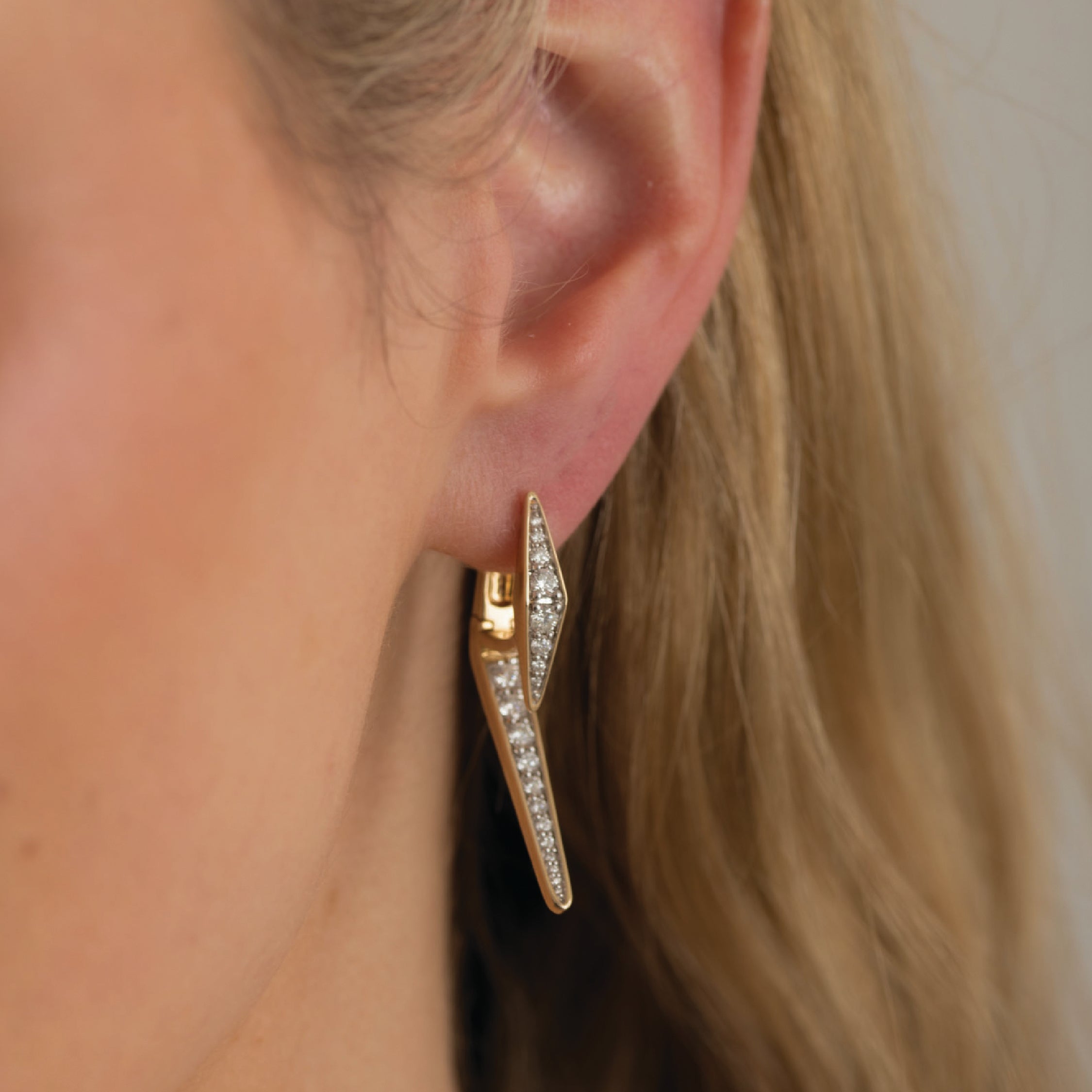 Closeup of 14K solid gold earrings with diamonds on an ear, showcasing elegant design.