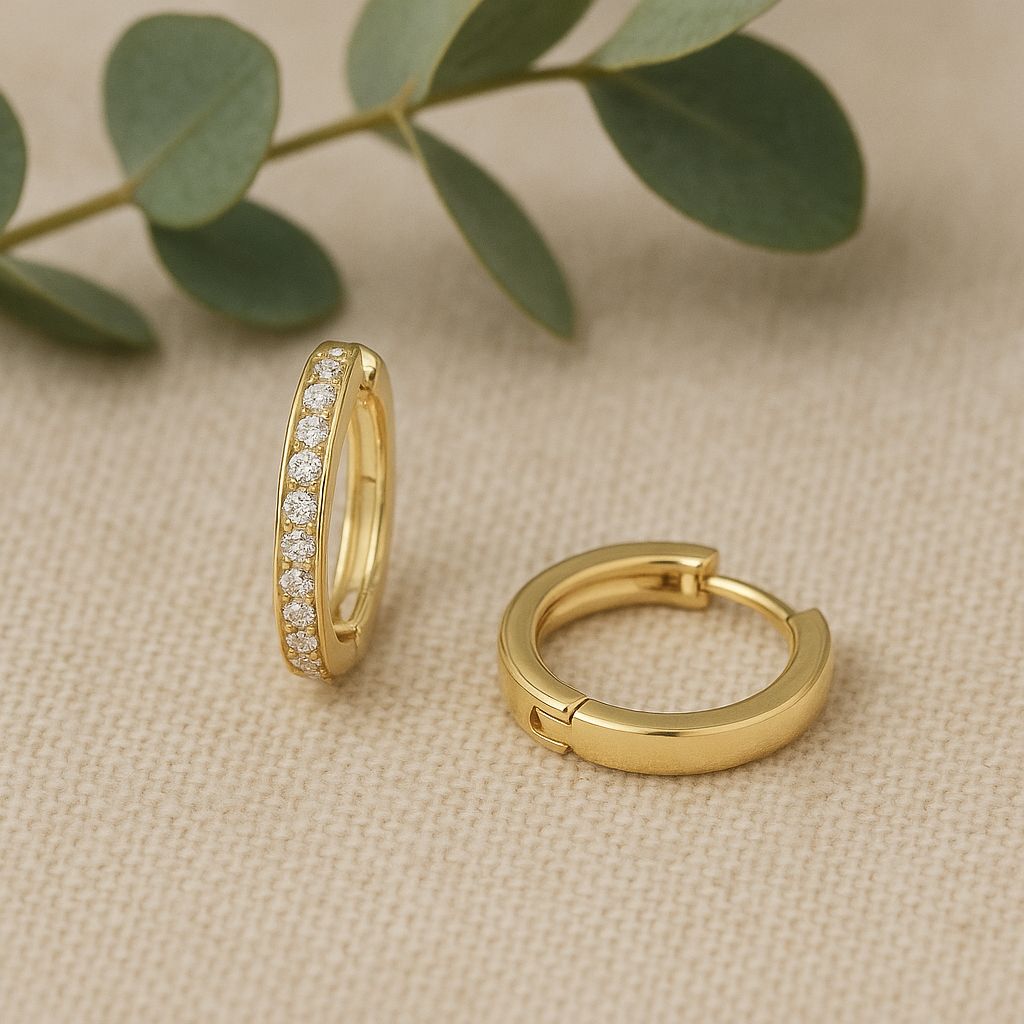 Gold hoop earrings on a beige fabric background with green leaves.