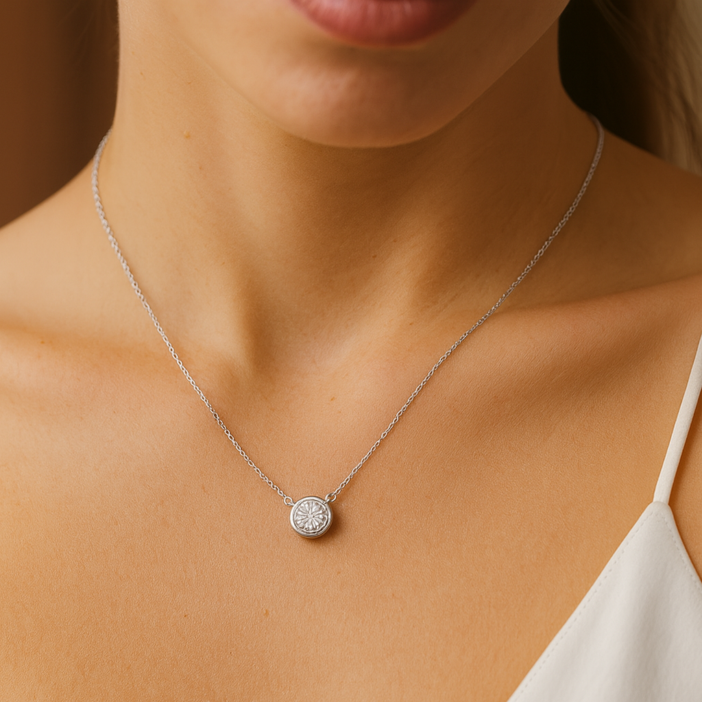 Silver necklace with a round pendant on a person wearing a white top.