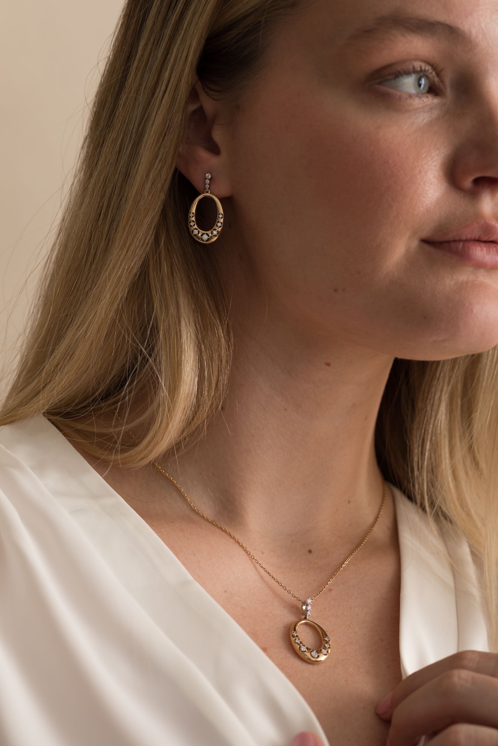Woman wearing 14K solid gold diamond necklace and earrings with a white blouse.