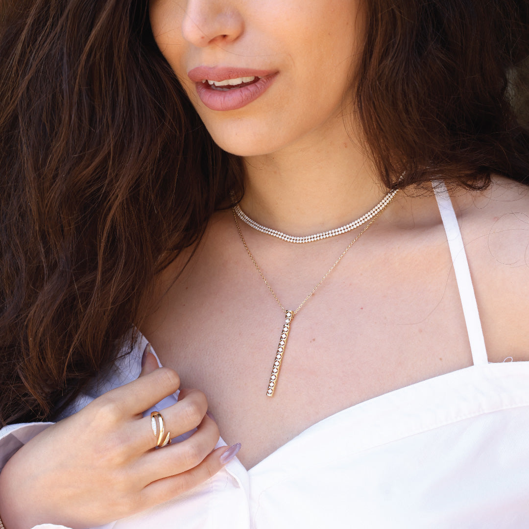 Woman wearing 14K gold diamond necklace with bar pendant and white top.