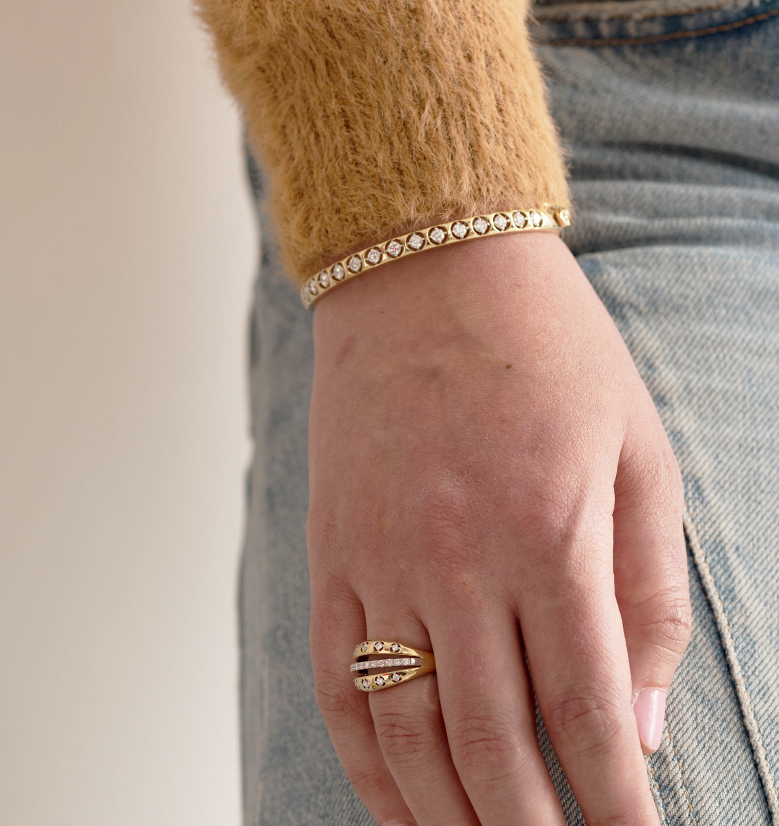 Hand wearing The Sydney 14K solid gold diamond ring and matching bracelet on denim.