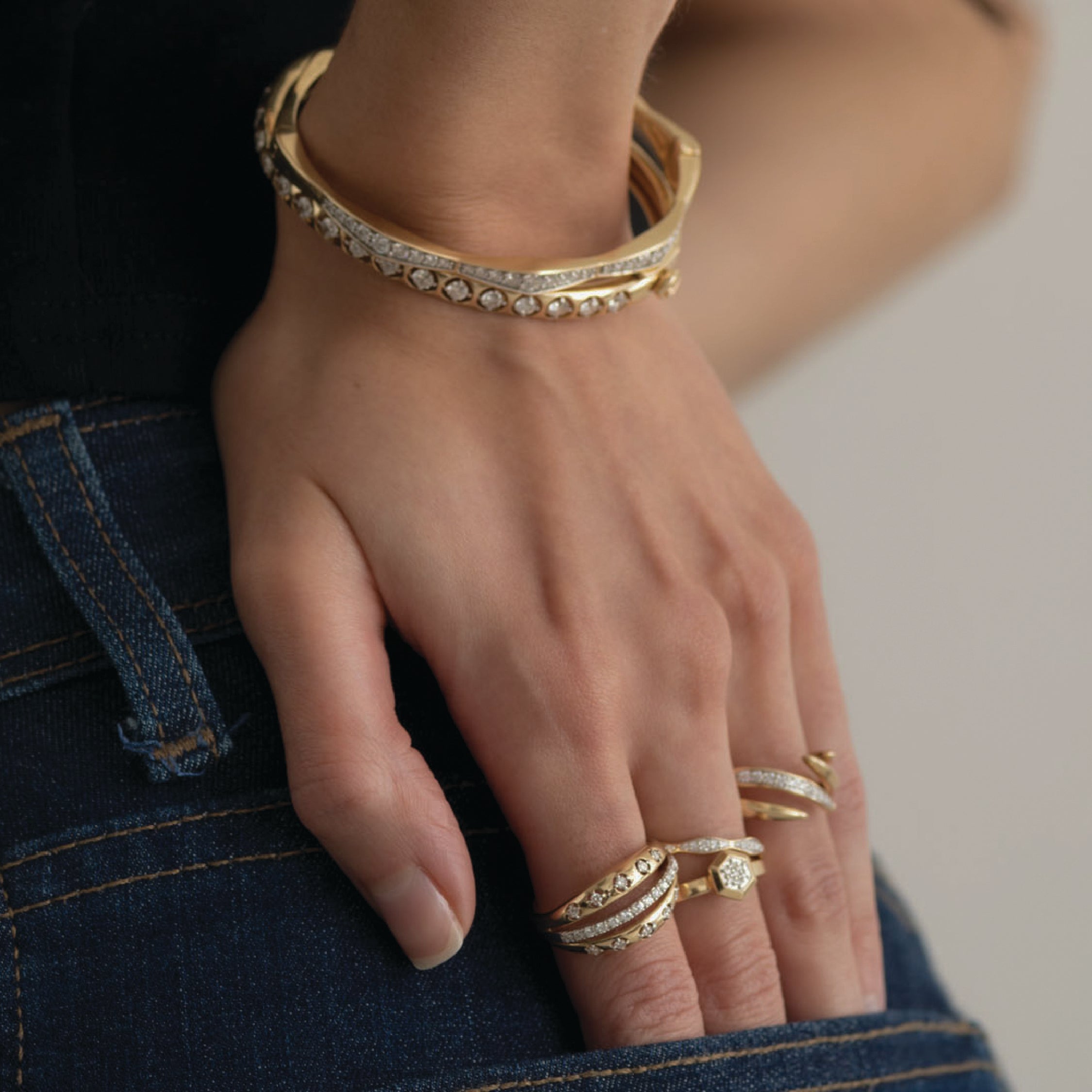Hand wearing 14K gold diamond rings with intricate designs and a gold bracelet.