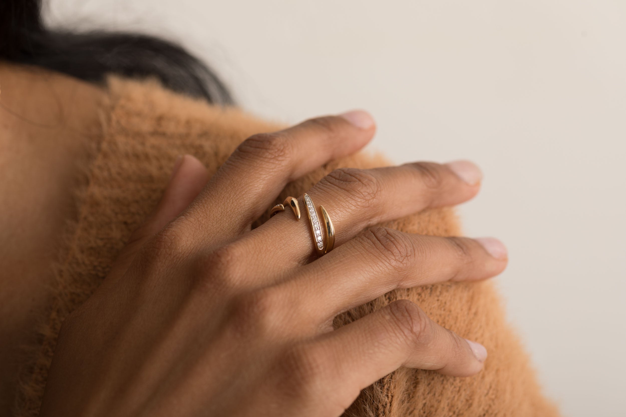 14K gold diamond swirl ring on hand with beige sweater background.