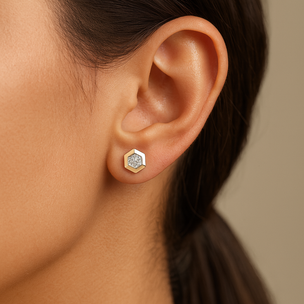 Close-up of an ear wearing a gold hexagonal earring with a clear gemstone on a neutral background