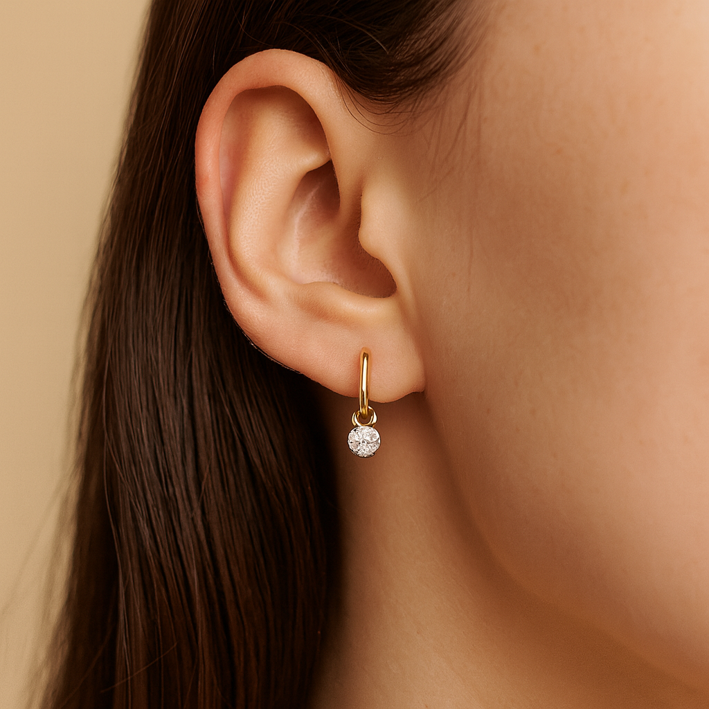 Gold earring with a small round gemstone worn by a person with long dark hair.