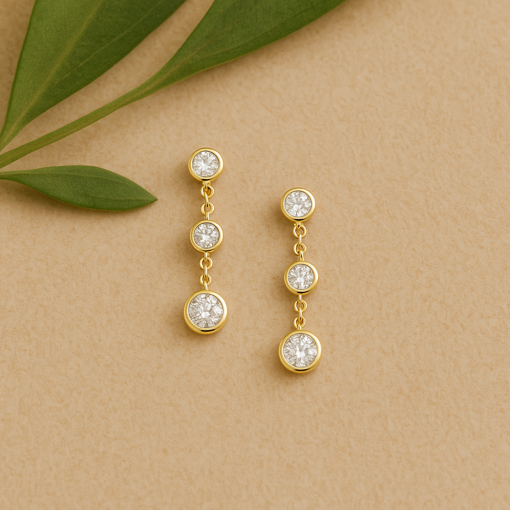 Gold earrings with clear stones on a beige background with green leaves.
