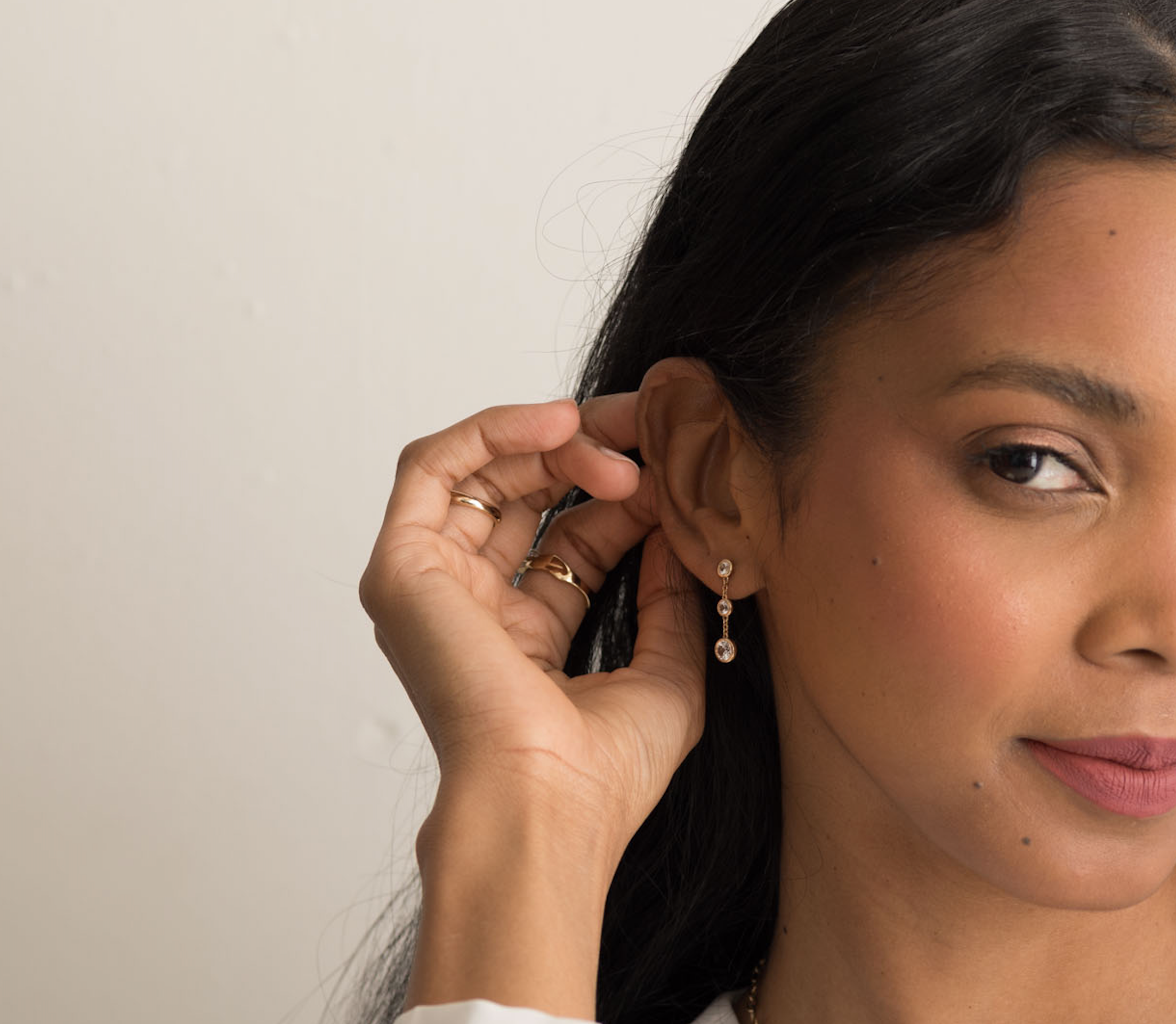 Woman wearing 14K solid gold earrings with white sapphire gemstones in a drop style.