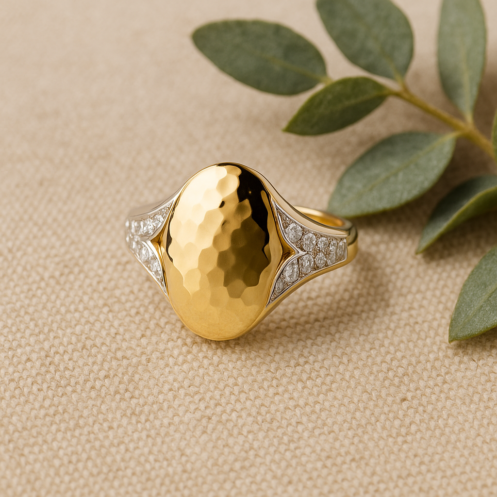 Gold ring with diamond accents on a beige fabric background with green leaves.