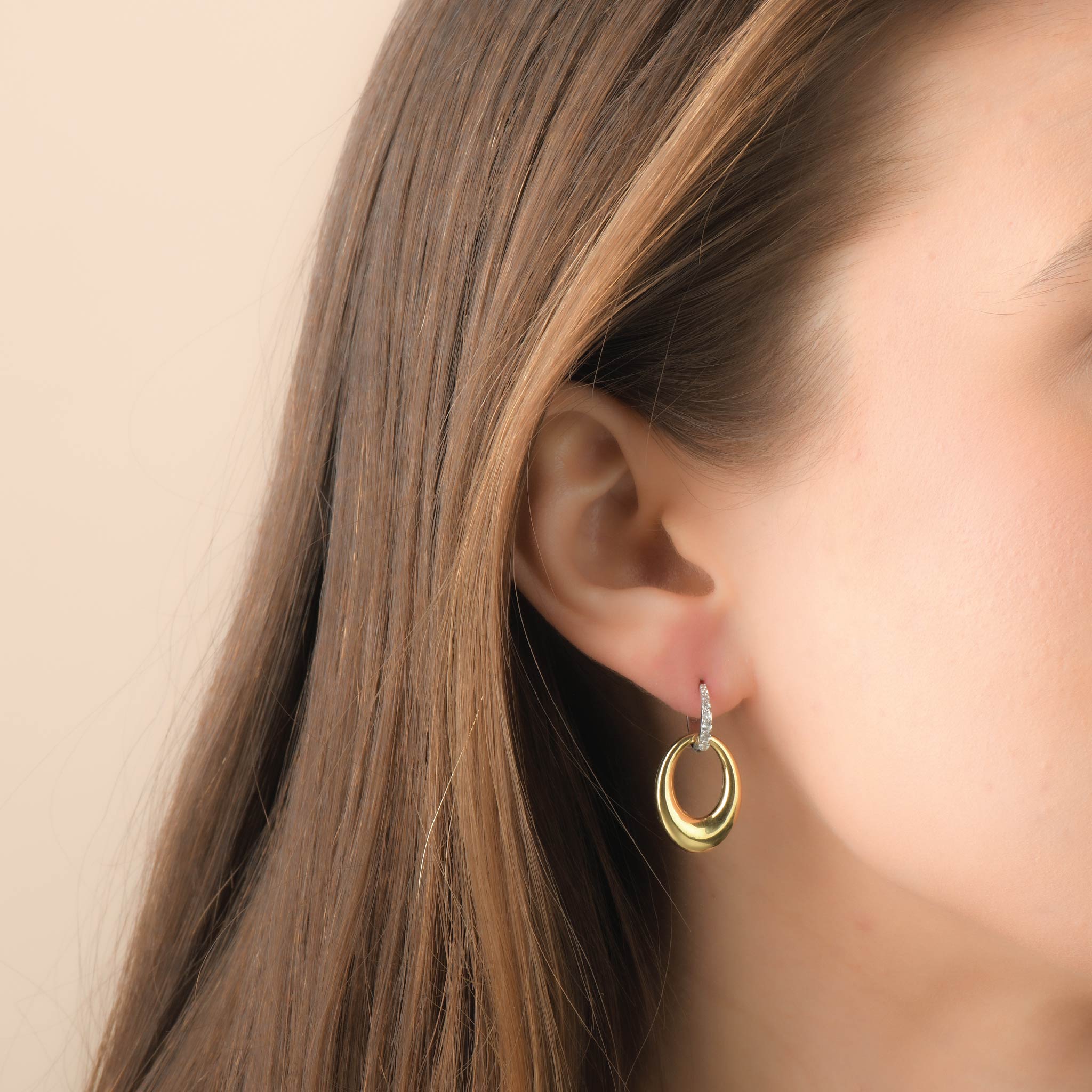 Close-up of gold and silver hoop earrings with white sapphires on a woman's ear.