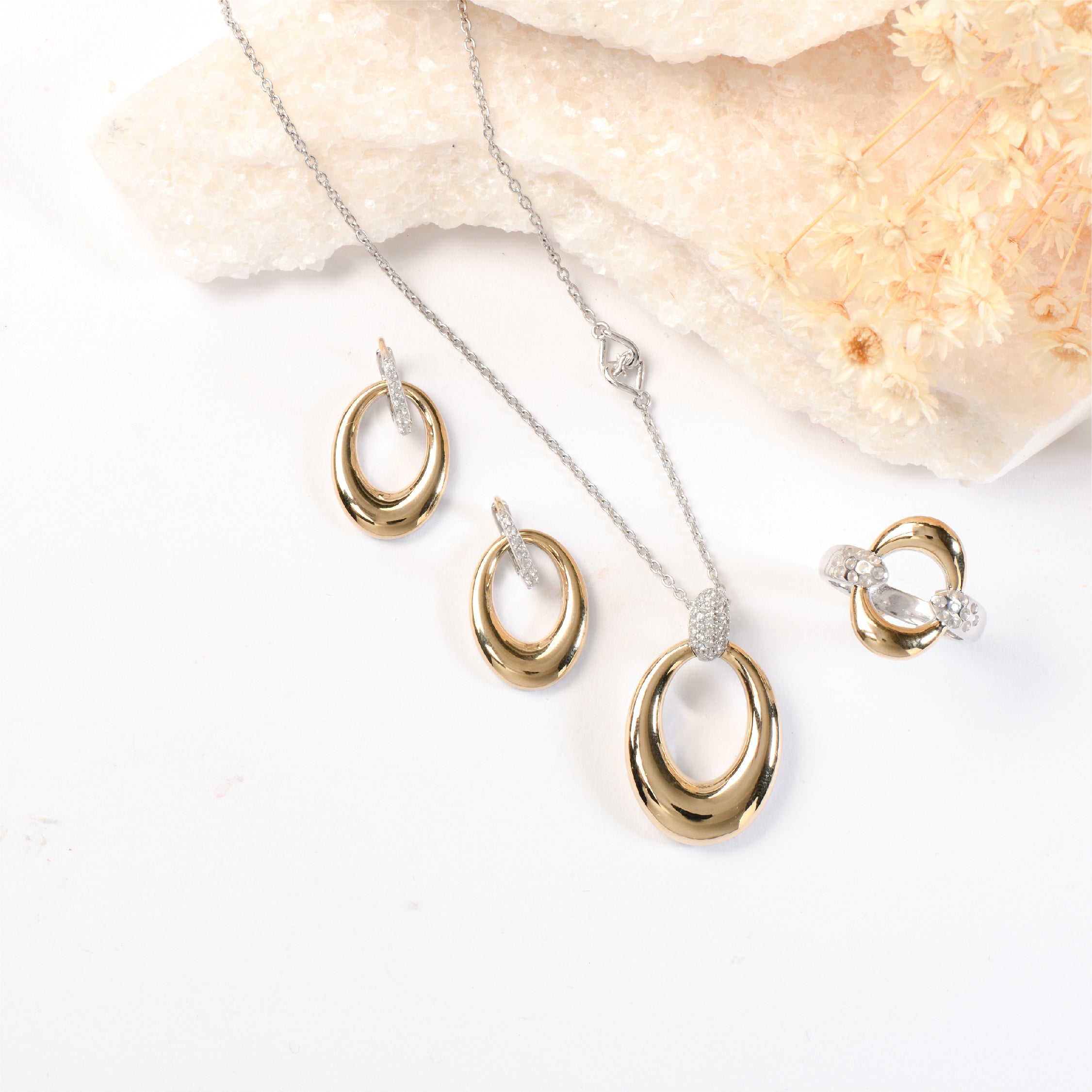 Gold and silver oval earrings and necklace set on a white background with floral accents.