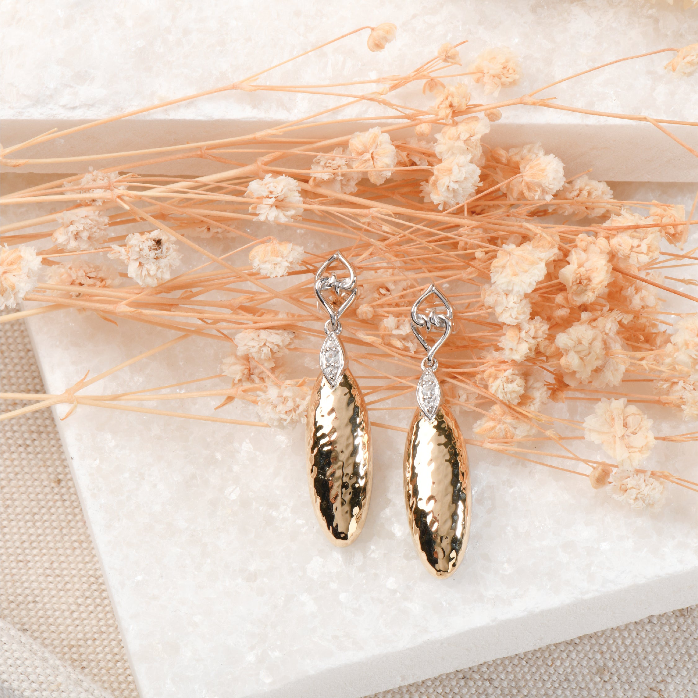 Hammered gold teardrop earrings with sterling silver and gemstones on floral background.