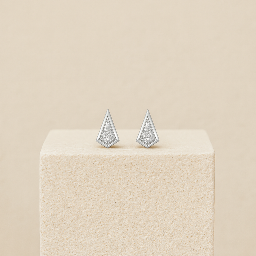 Pair of silver triangle earrings on a beige pedestal against a beige background