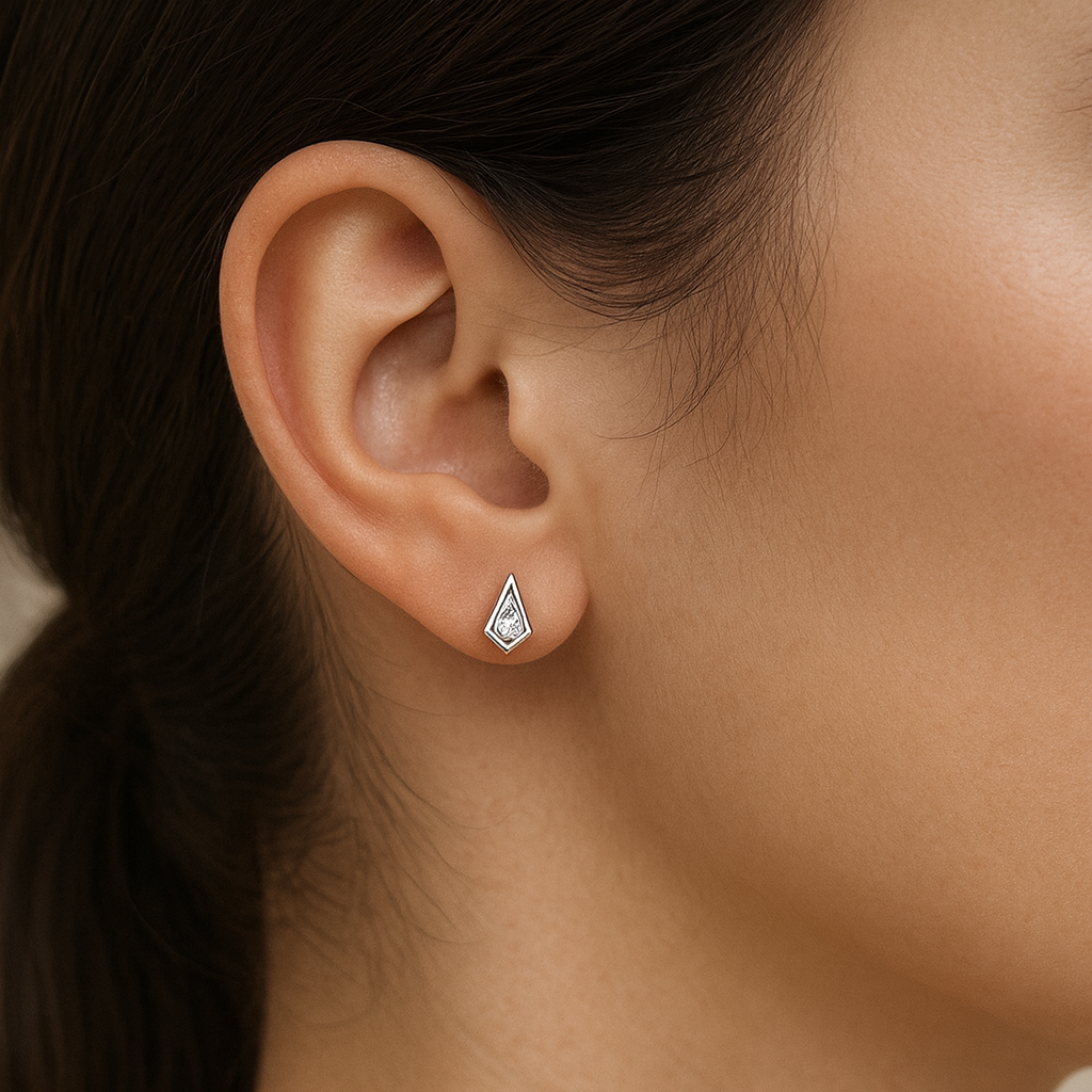 Close-up of a person wearing diamond stud earrings with a neutral background