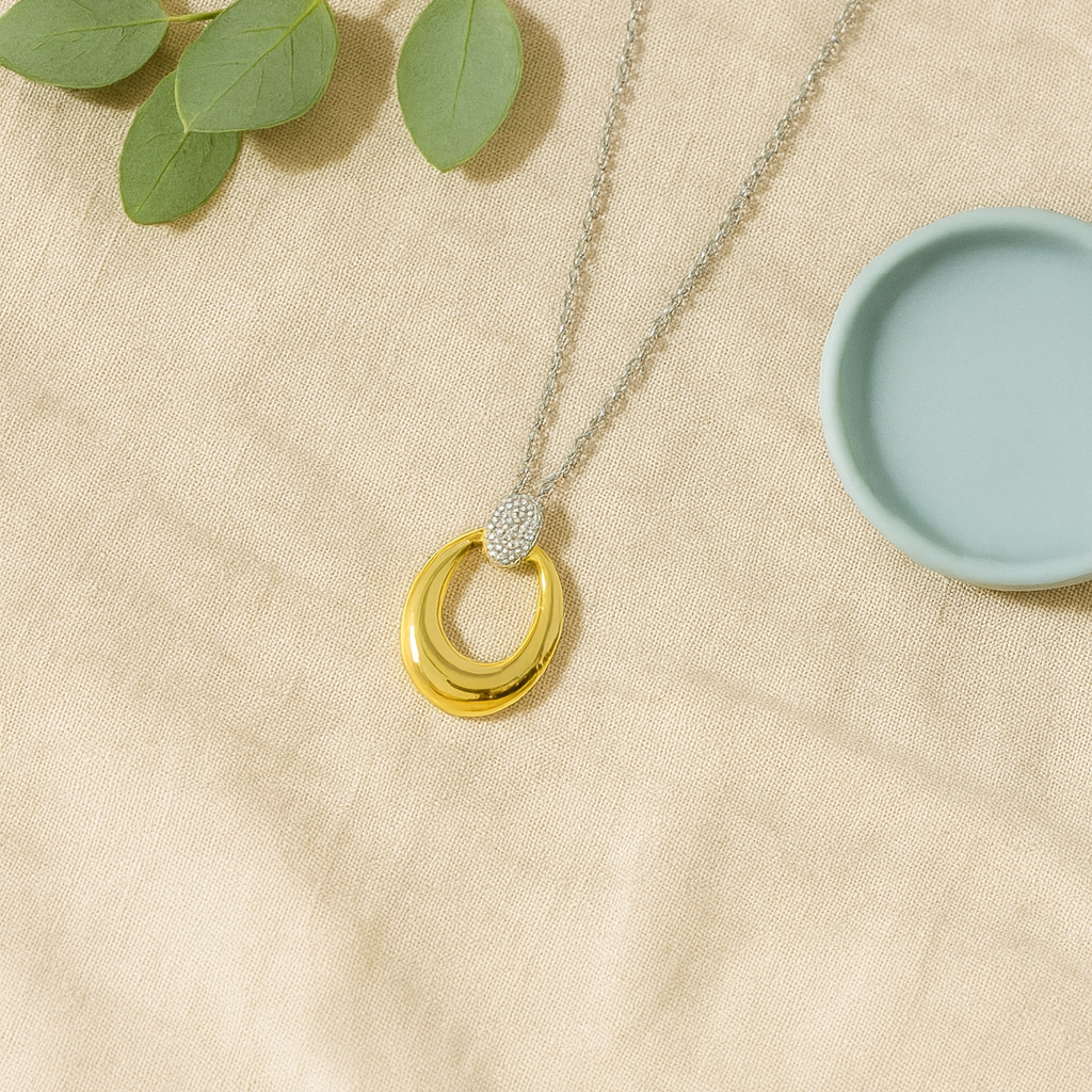 Necklace with gold rings on a beige surface with green leaves and a blue dish.