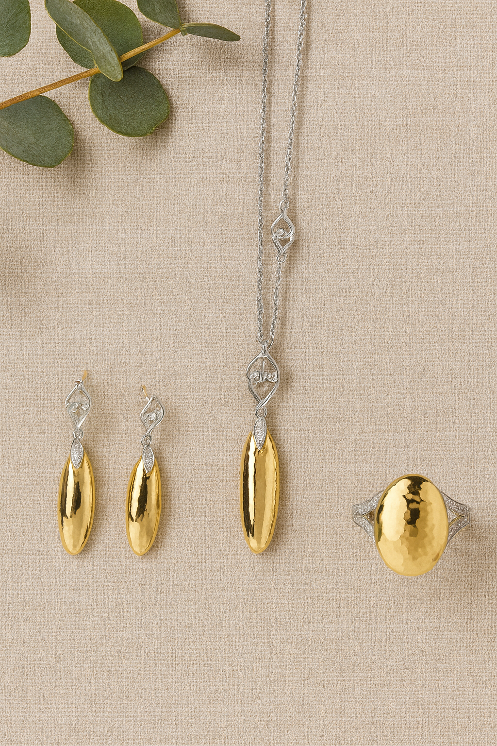 Gold and silver jewelry set on a beige surface with green leaves.