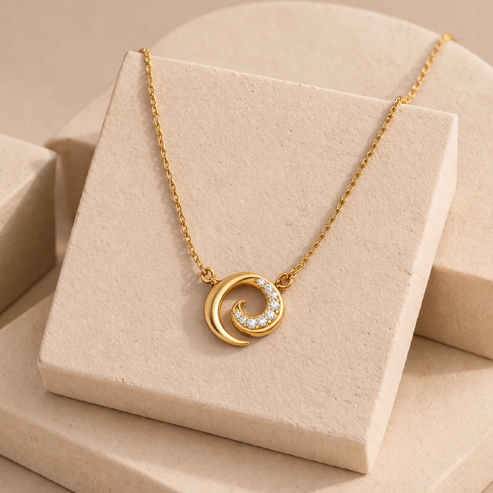 Gold necklace with a crescent moon and diamond design on a beige display stand.