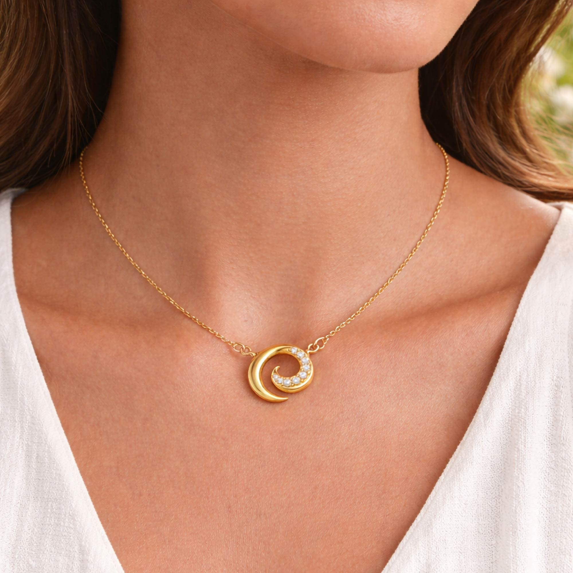 Gold necklace with a circular pendant worn by a person in a white top.