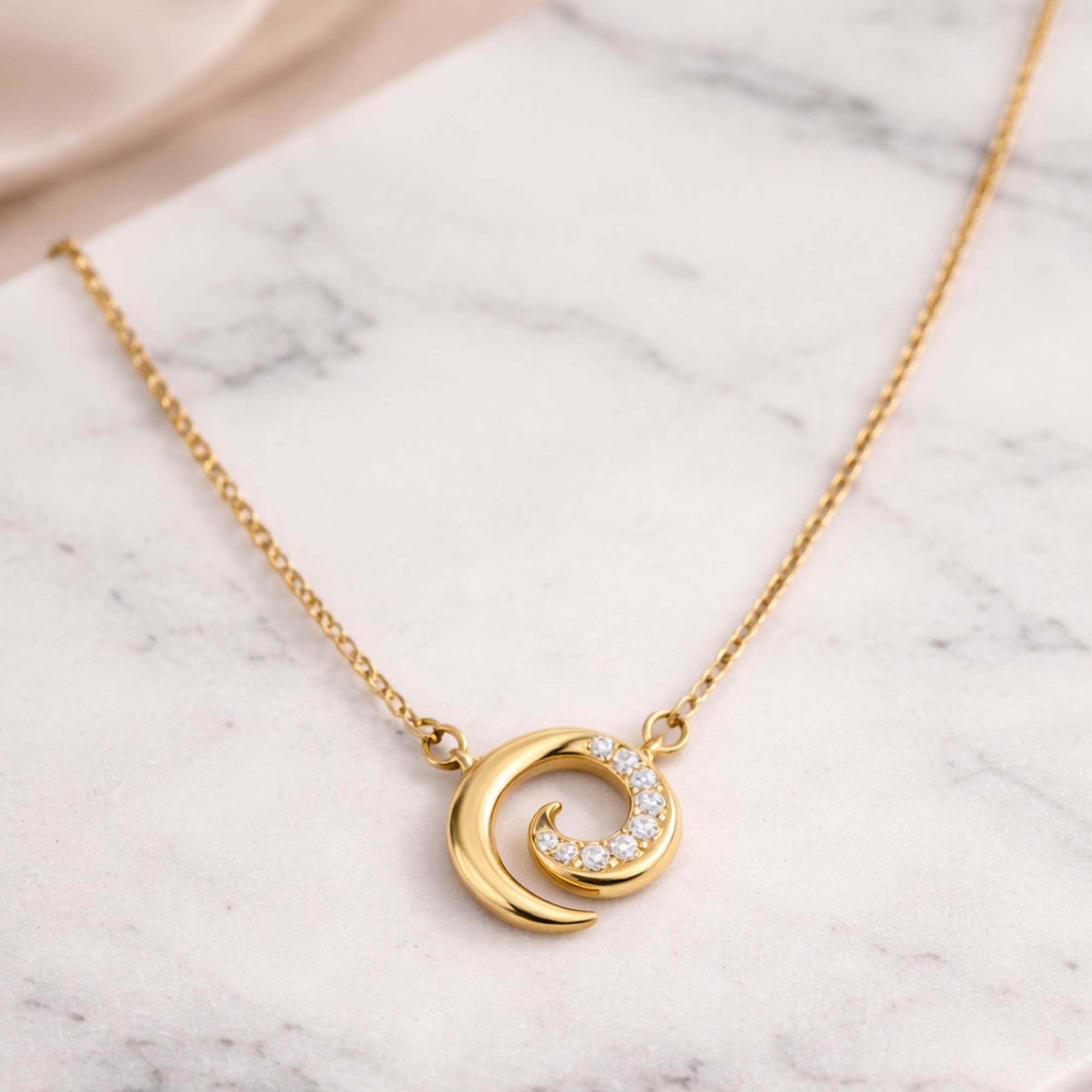 Gold necklace with a crescent moon pendant on a marble surface